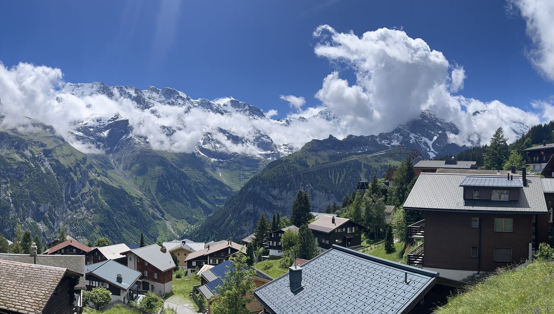 Snowcapped Alpine peaks above a green mountain village under a bright blue sky